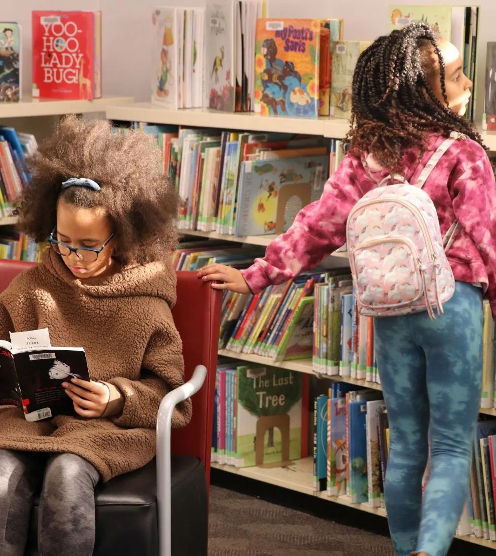 A woman wearing a mask and two young children looking at library books.
