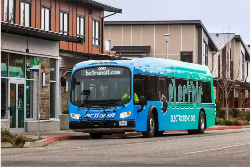 A blue and green electric demonstration bus parked in a residential area