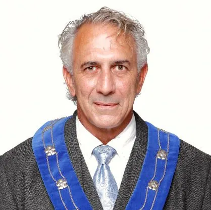 Portrait of Mayor Sid Tobias wearing a ceremonial mayoral chain over a grey suit jacket and blue tie