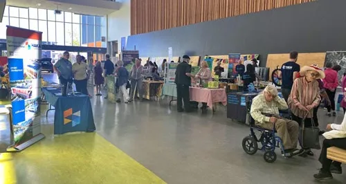 A community gathering or fair with information booths inside a large hall