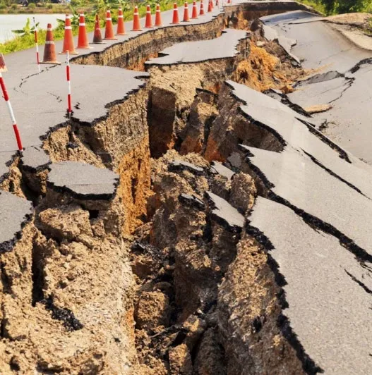 A photograph of a severely cracked and damaged asphalt road, possibly after an earthquake