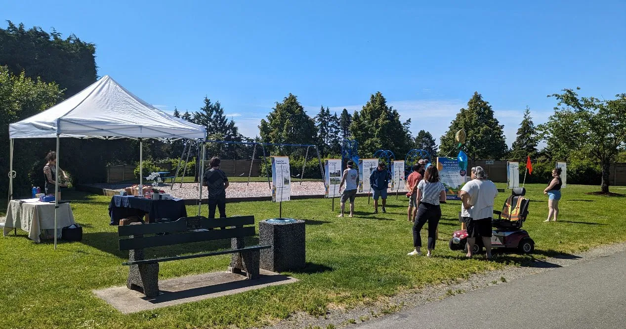 A community engagement event held outdoors at Chancellor Park, featuring a white canopy tent, informational display boards, and community members interacting with staff.