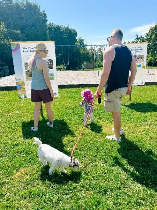 A photo showing a man, a woman, a small child, and a dog on a leash participating in an outdoor public consultation event at the park.