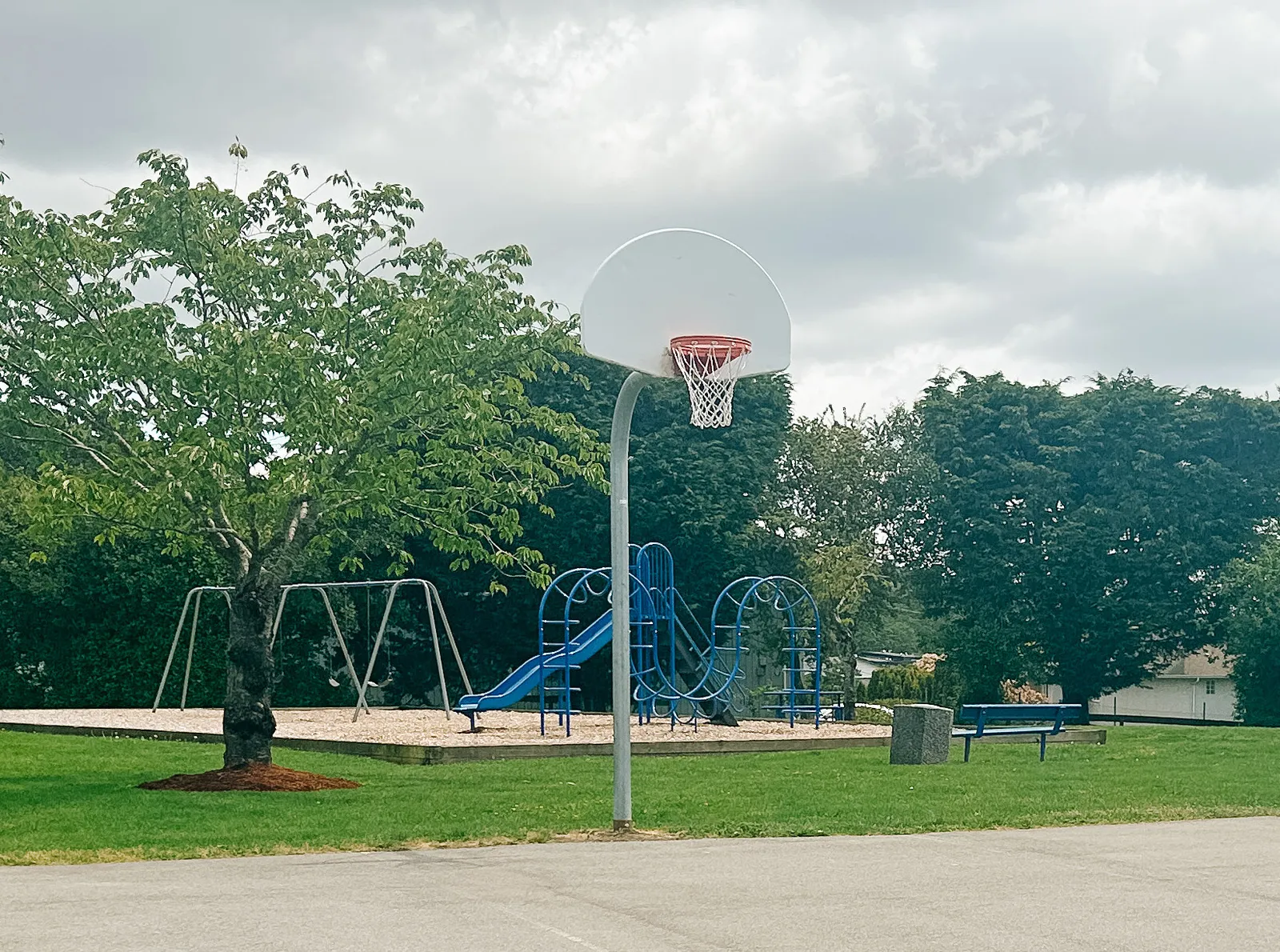 Photo of the existing Chancellor Park playground with a blue play structure and a basketball hoop