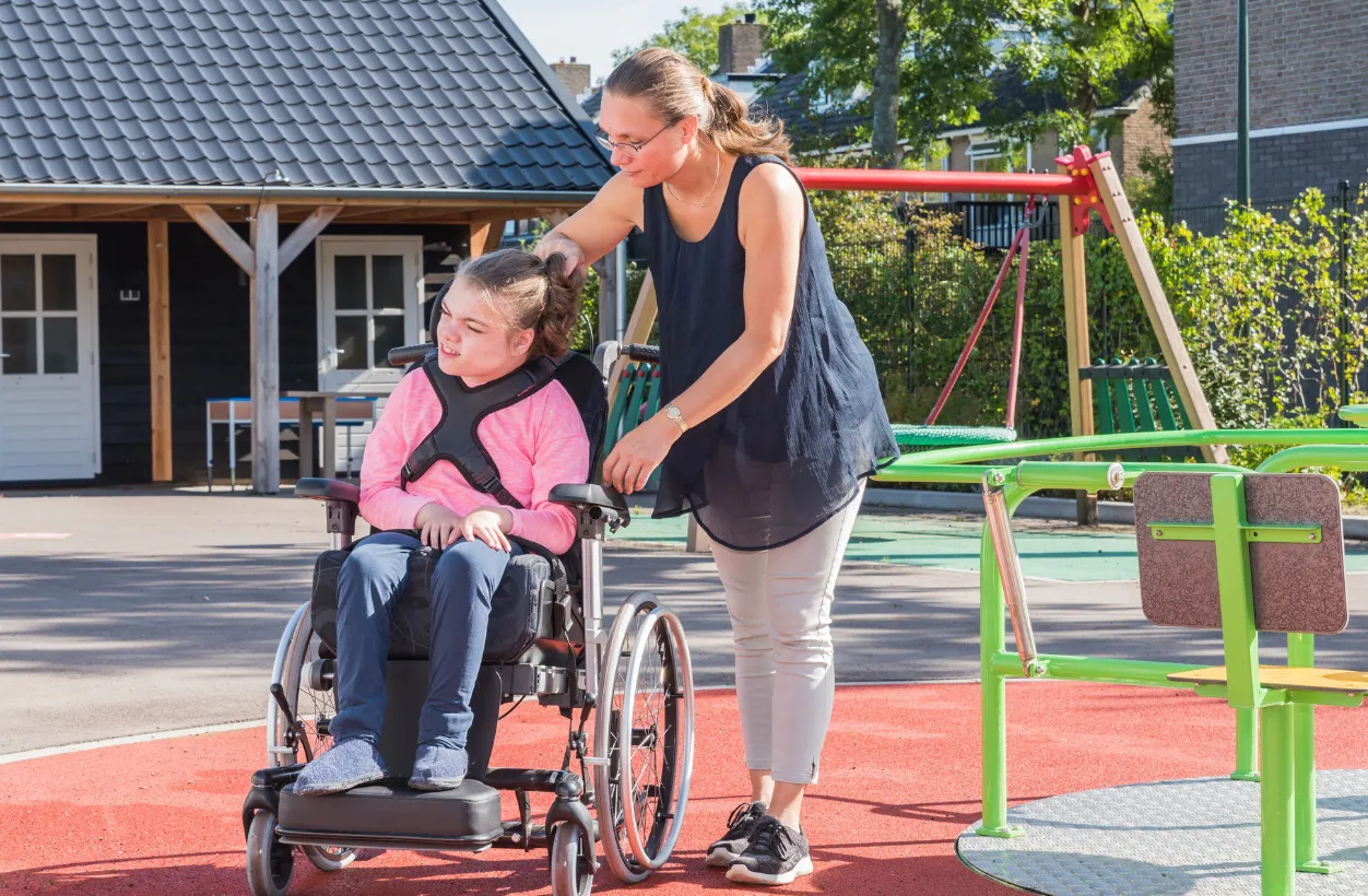 A woman assisting a child in a wheelchair on an accessible merry-go-round