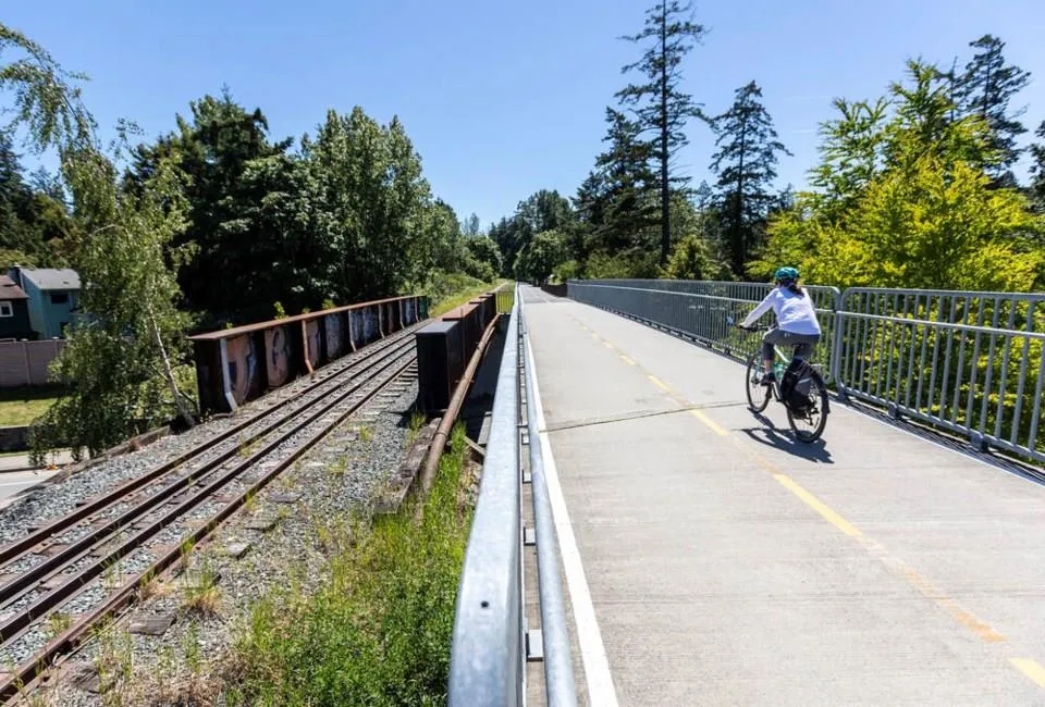A person cycling along the paved E&N Trail, which runs parallel to a set of railway tracks.