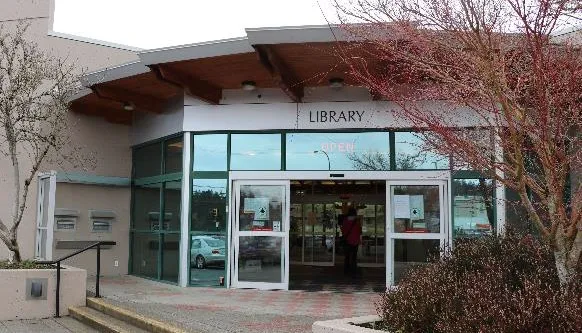 People lining up to enter a library branch, with a "Hello again!" sign visible on the glass.