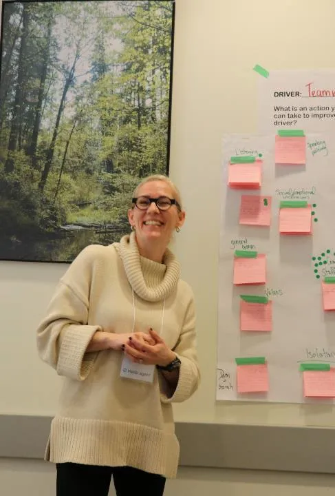 A library staff member standing in front of a whiteboard filled with colorful sticky notes used for community planning.