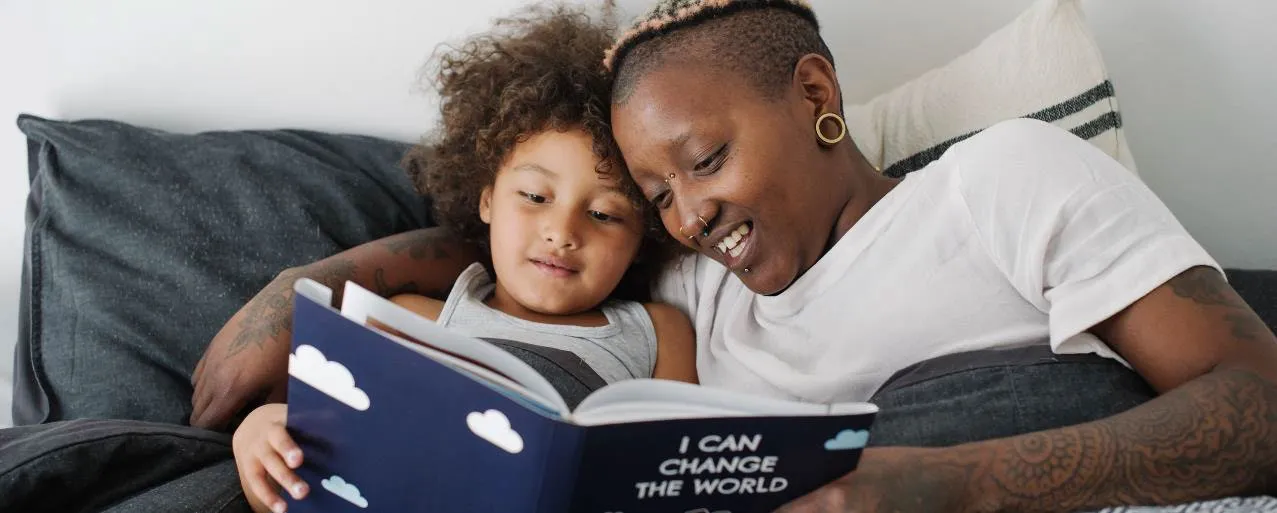 An adult and a young child lying in bed together, reading a book titled "I CAN CHANGE THE WORLD."
