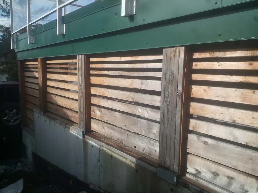 Exterior wall with wooden slats over building wrap and a concrete foundation