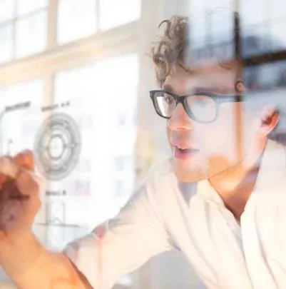 A man in glasses looking through a glass pane with technical drawings