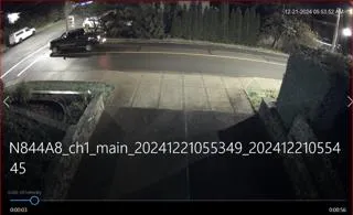 Low-light security camera screenshot showing a street at night with parked vehicles and an overlay of file metadata