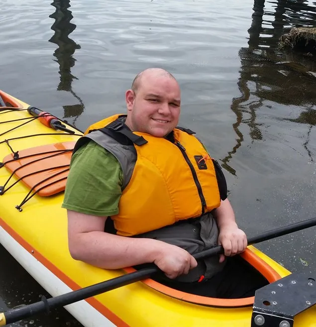 A man wearing an orange life jacket sitting in a yellow kayak on the water