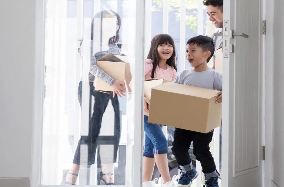 A smiling family carrying cardboard boxes into a new home