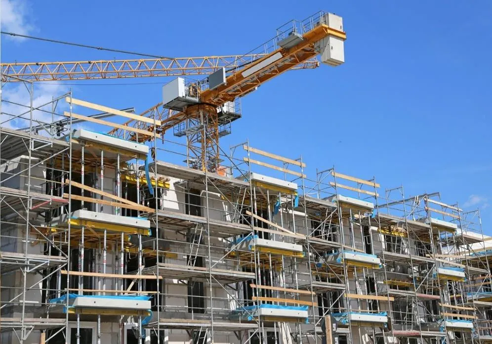 A large multi-story residential building under construction with scaffolding and a yellow crane