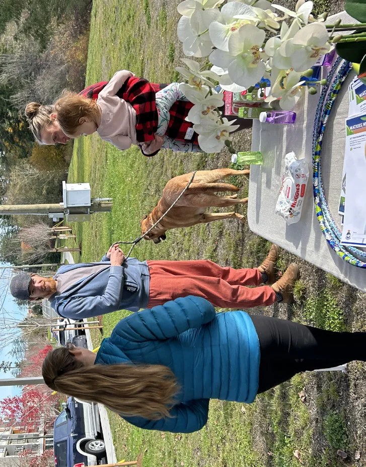 A local resident and child with a dog visit an information table set up at the future park site during an outdoor engagement event