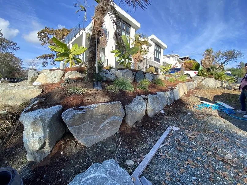 Photo showing tiered boulder retaining walls and landscaping along the property line