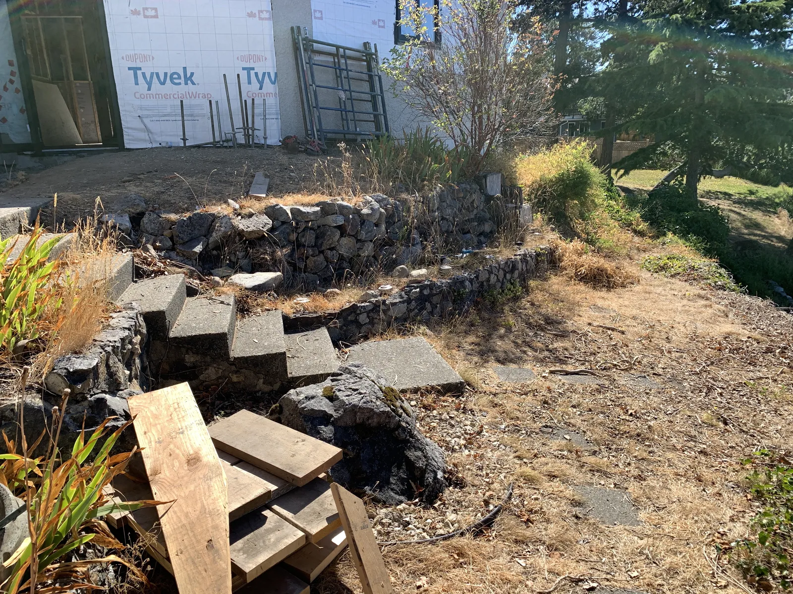 Mortared rock wall with concrete steps leading up to a house under construction with Tyvek wrap