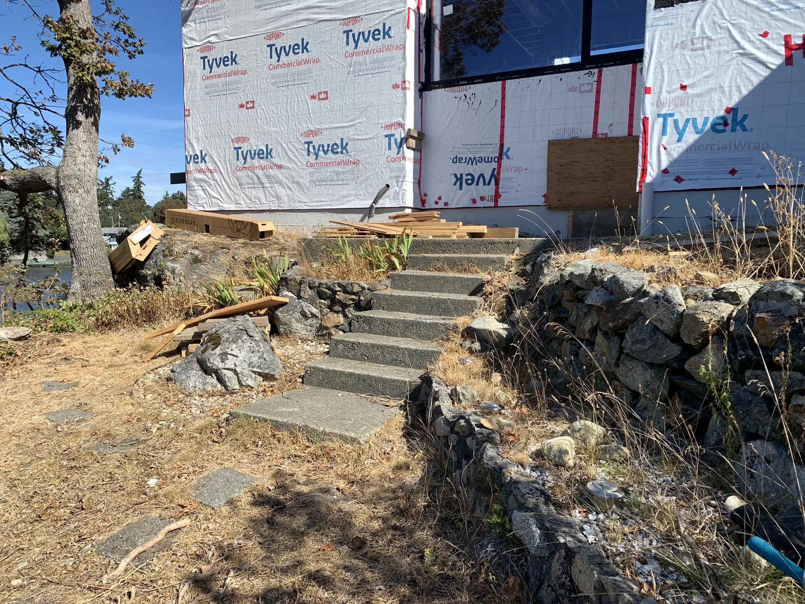 Concrete steps and mortared rock wall at the base of a building covered in Tyvek wrap
