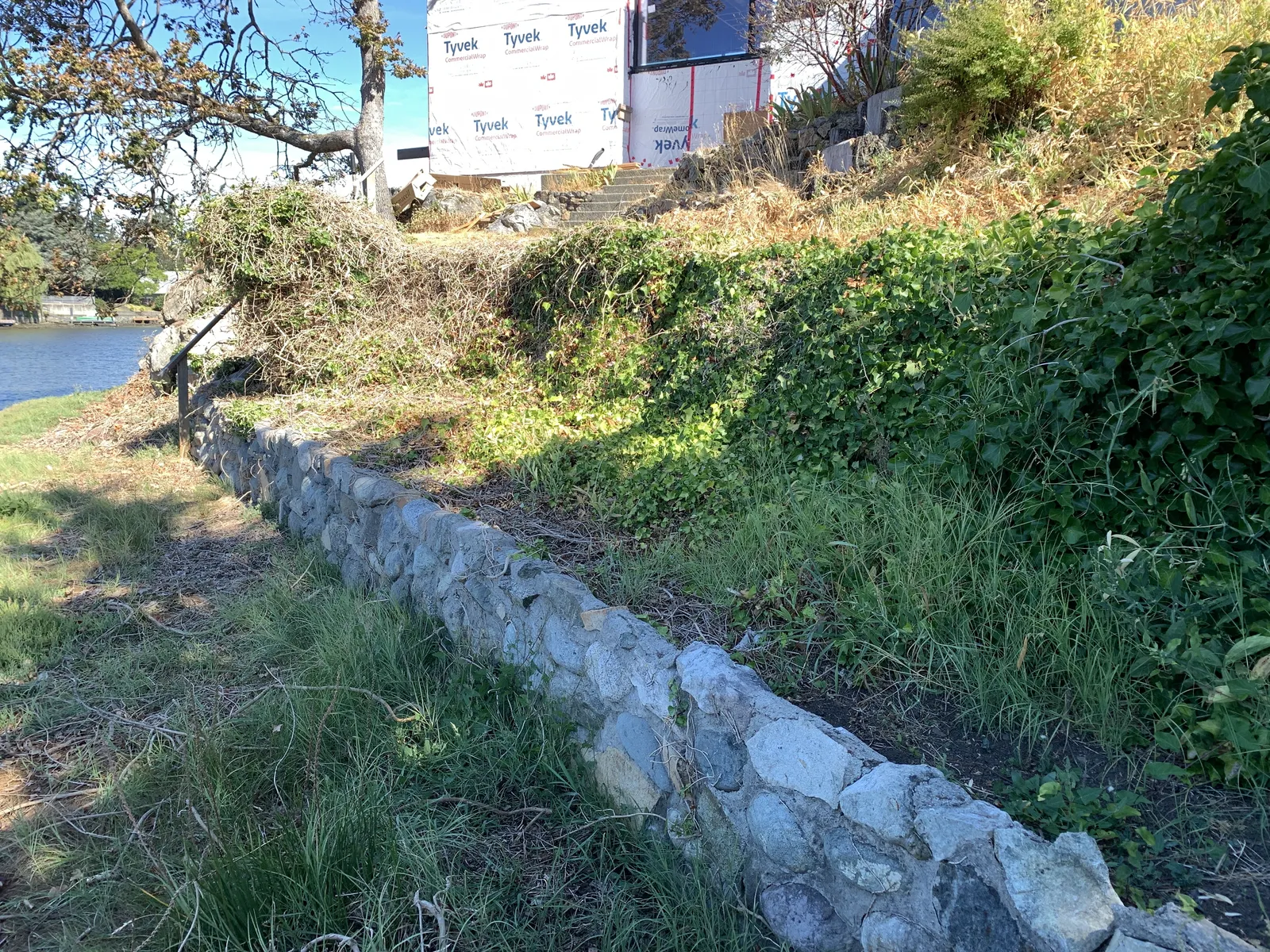 Long mortared stone retaining wall on a vegetated slope leading down towards the water
