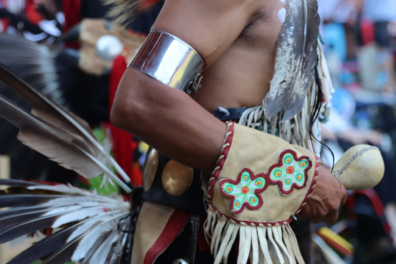 Close-up of a dancer's regalia including a silver arm band, beaded pouch, and feathers