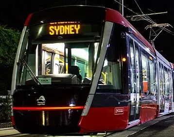 Nighttime photo of a modern red and black tram displaying "SYDNEY" on its destination board