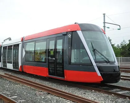 Close-up profile of a modern red and charcoal light rail vehicle stationary on tracks