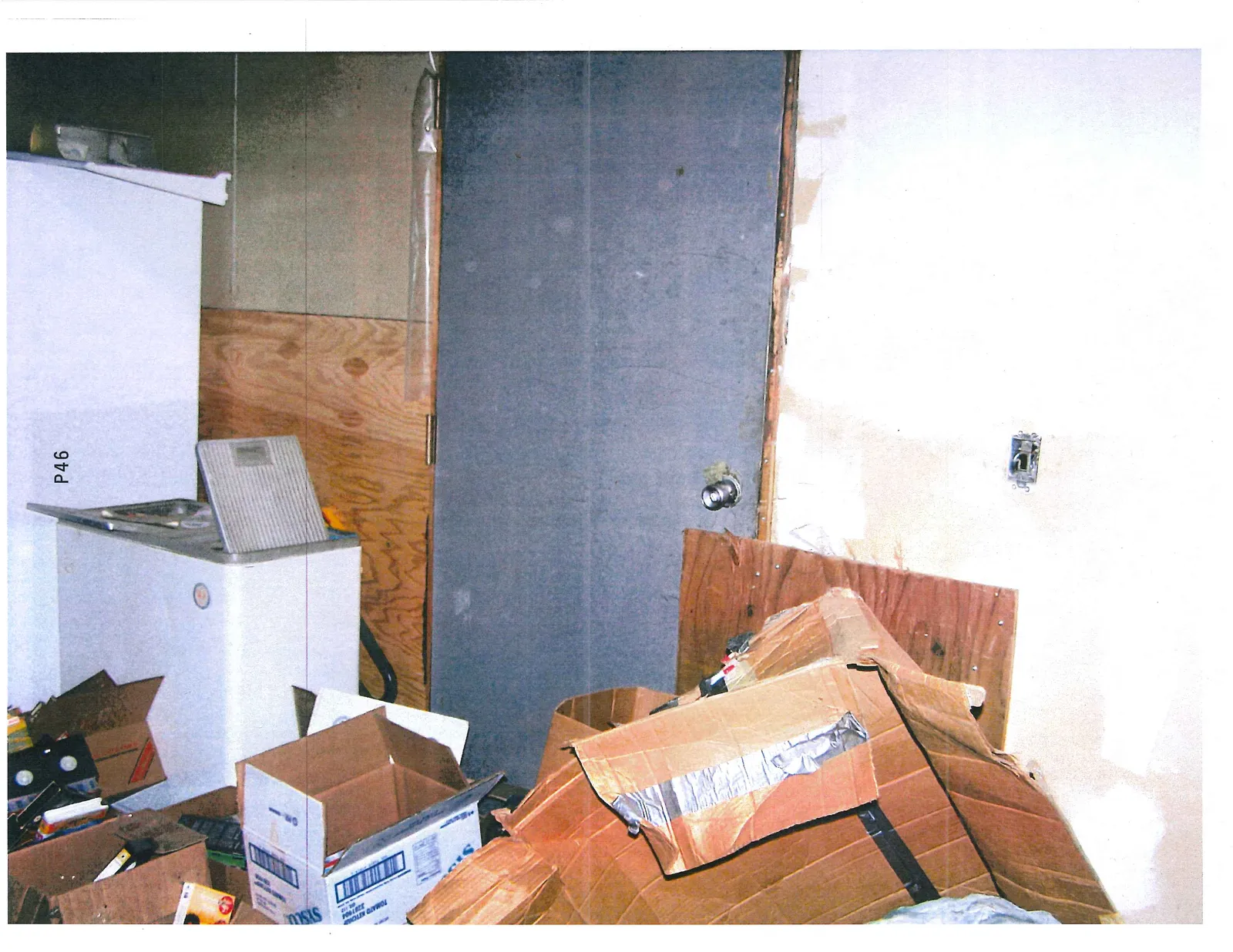 Cluttered interior room with a door panel lying on the floor and various boxes