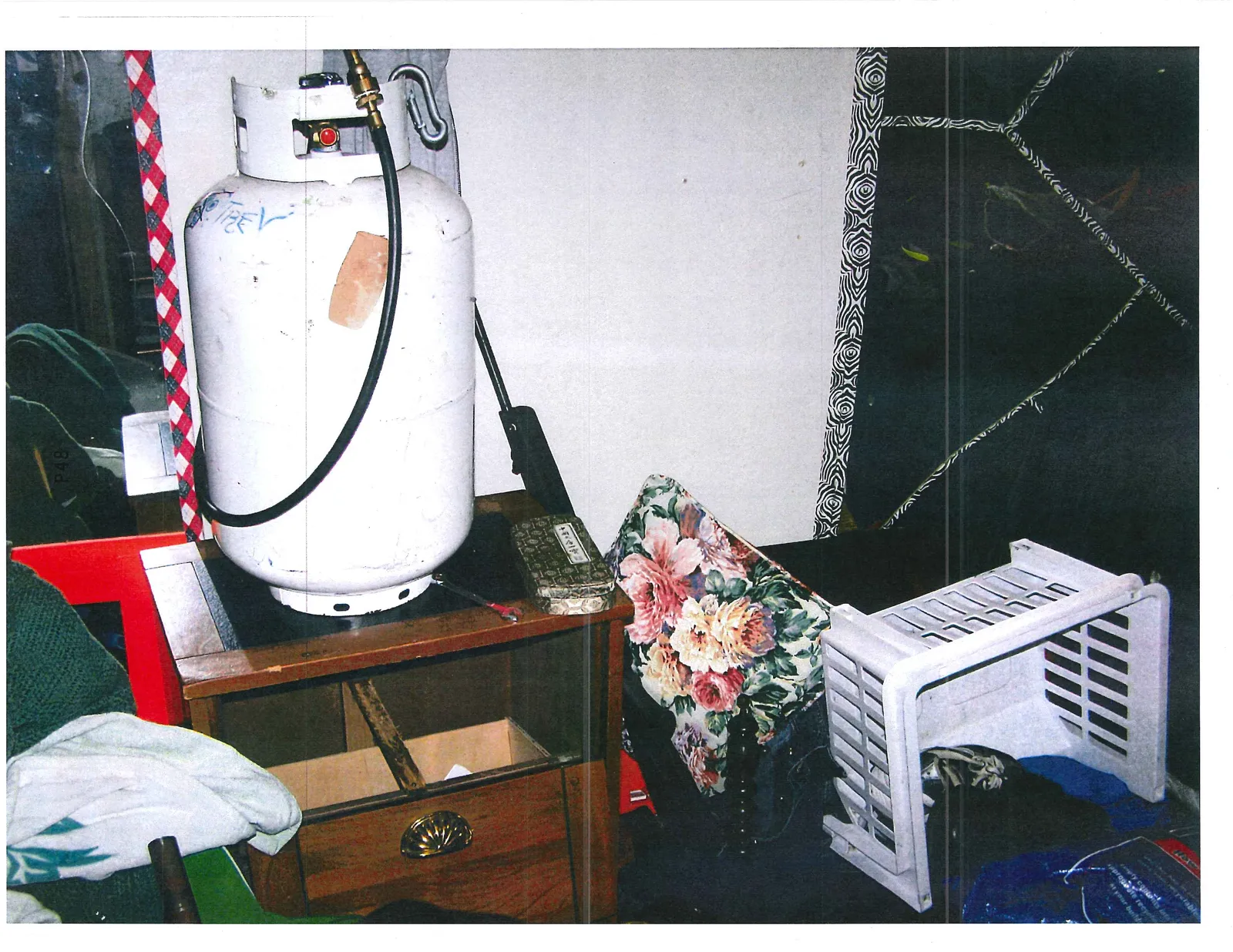 White propane tank stored indoors on a wooden stand next to personal items