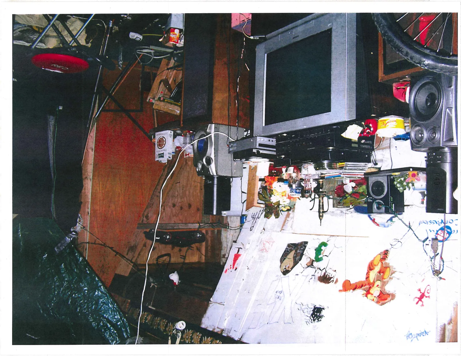 Heavily cluttered room with electronics, wall drawings, and tangled cables