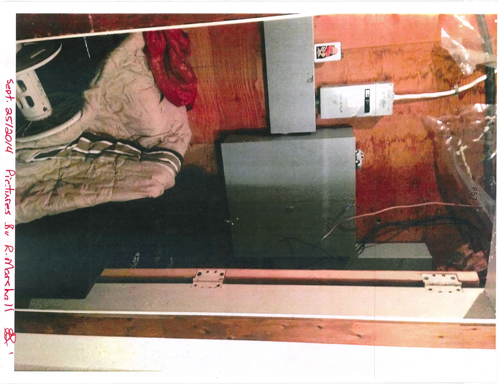 Utility room with electrical panels on a plywood wall, a white blanket, and a red cloth.