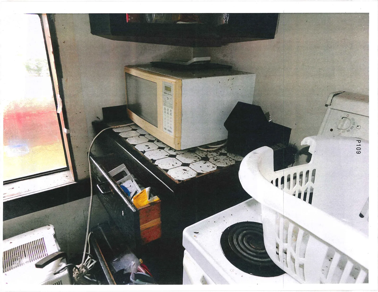 Messy kitchen area featuring a microwave on a tiled counter, a stove, and a white laundry basket