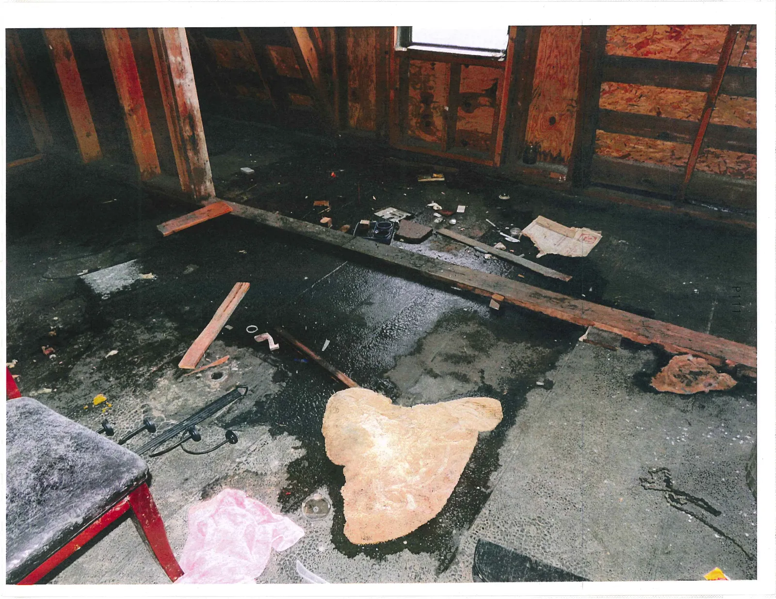 Interior room under construction with exposed wooden framing and debris scattered on a dark floor