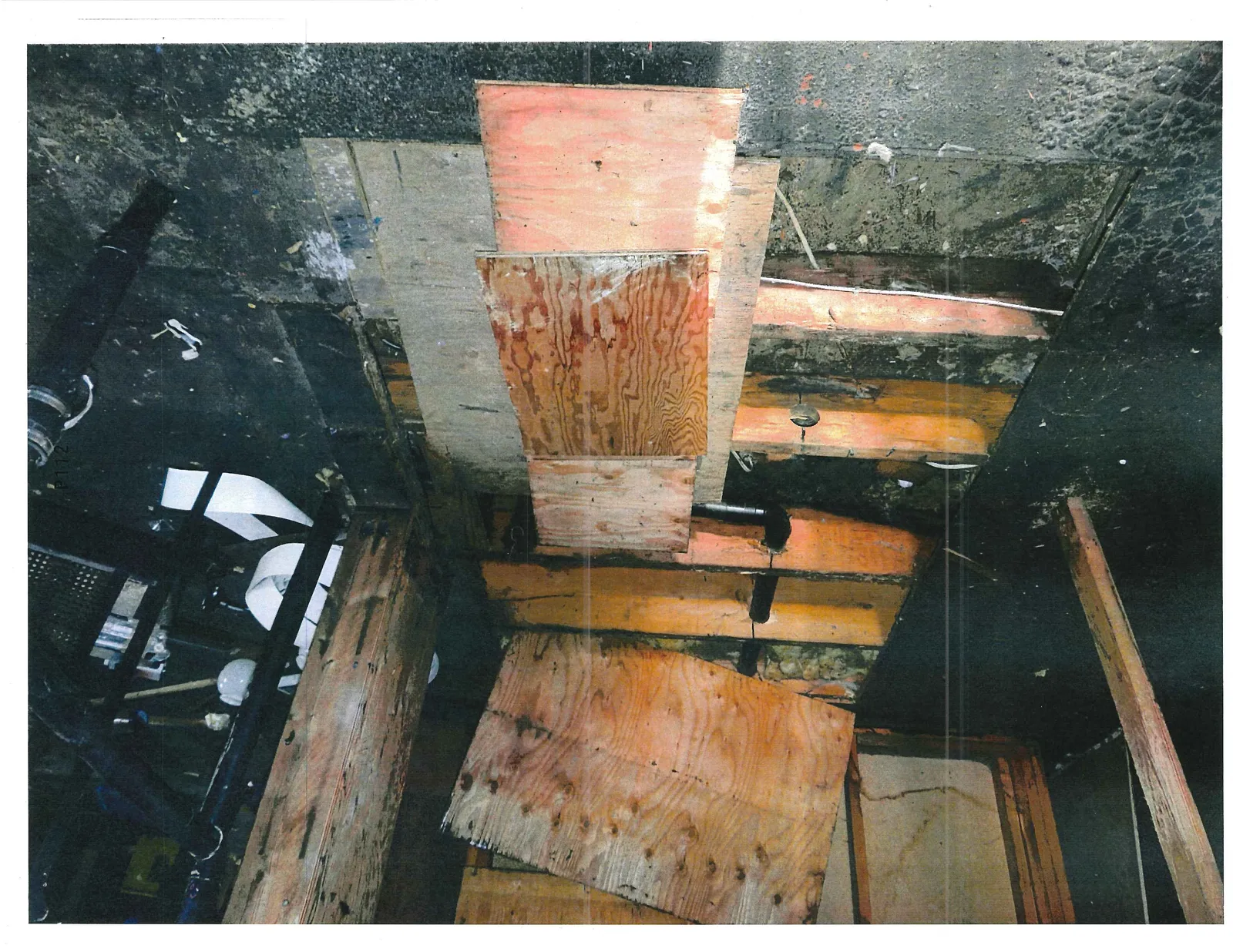 Detail view of exposed floor joists with plywood patches and plumbing pipes