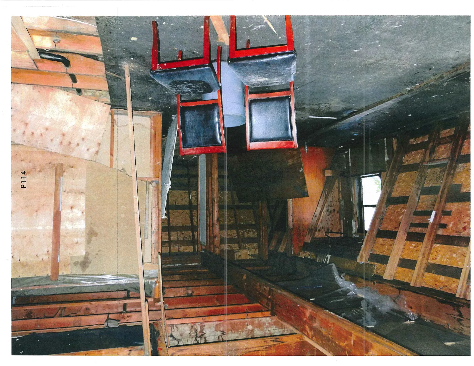 Interior room with exposed wooden studs and floor joists, featuring two chairs on a dark floor