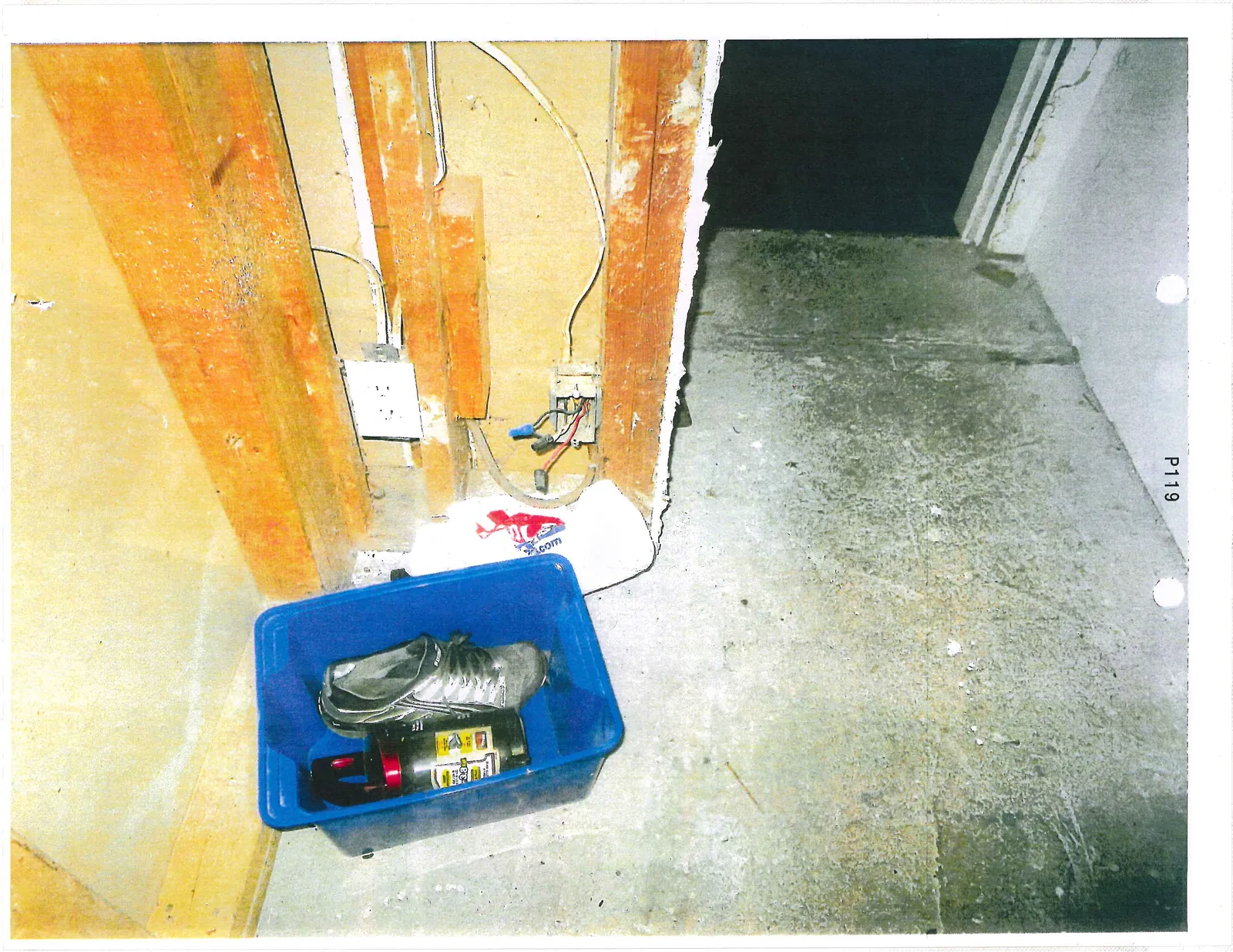 Exposed wall framing with an electrical outlet, an open junction box, and a blue bin containing personal items including a shoe and a bottle