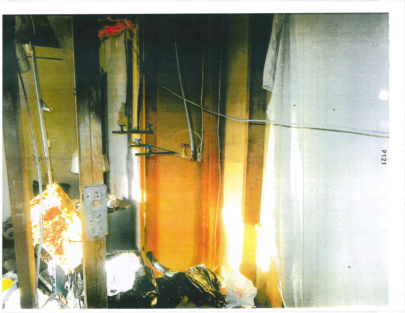 Interior space with exposed wall studs, plumbing pipes with valves, and debris including black trash bags
