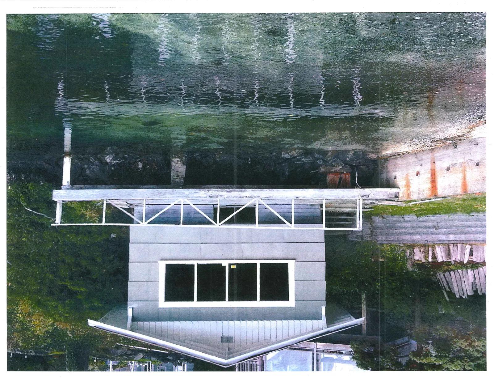 A light-grey waterfront building with a white gabled roof and a white wooden railing featuring an X-pattern design.
