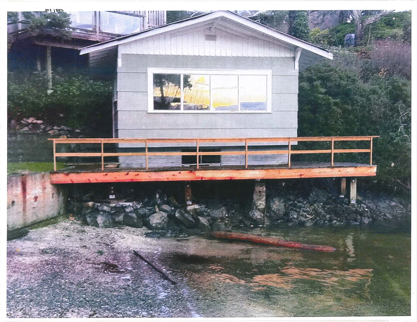 The same light-grey waterfront building with a newly constructed, unpainted wooden railing and deck frame.