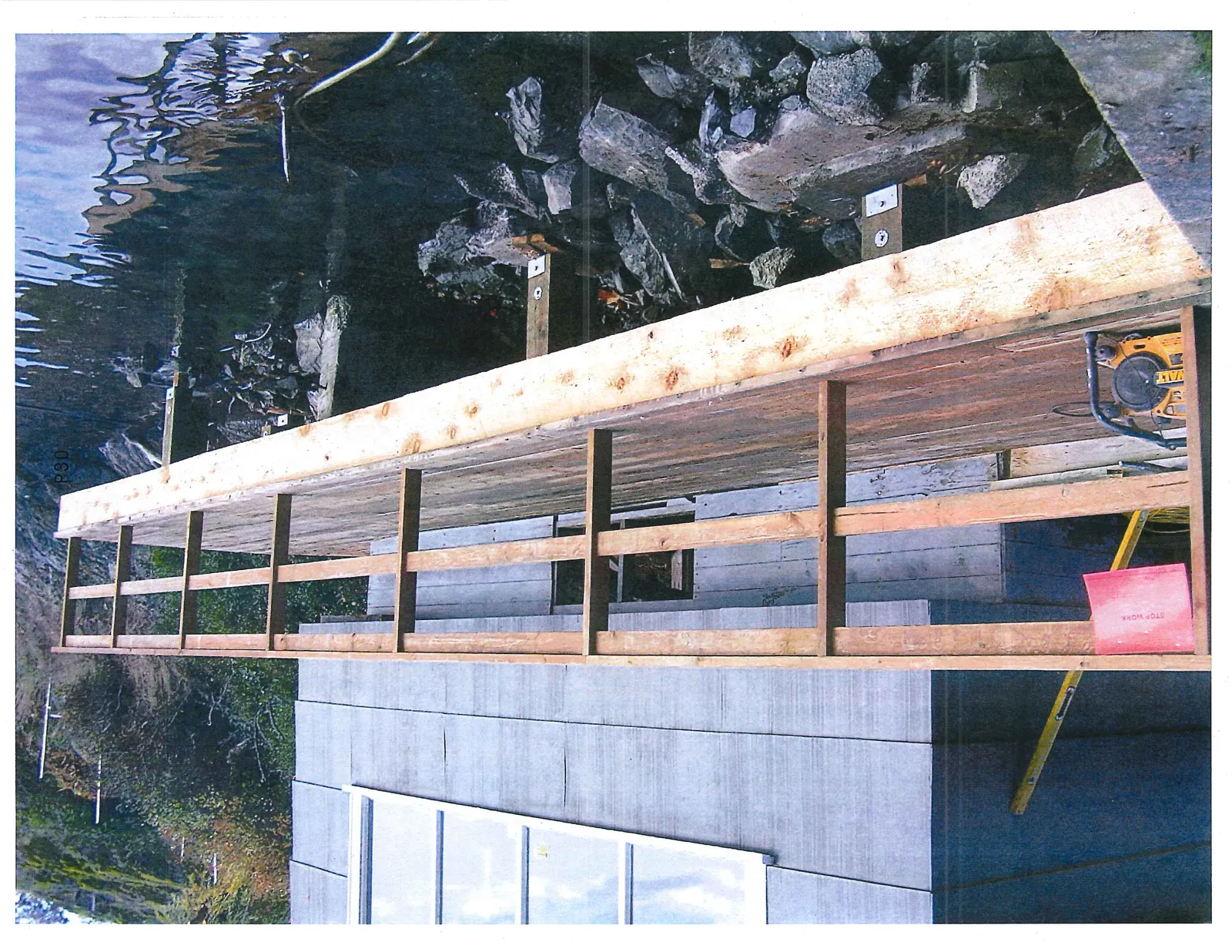 A close-up view of the new wooden deck framing under construction, featuring a red "STOP WORK" notice and construction tools.