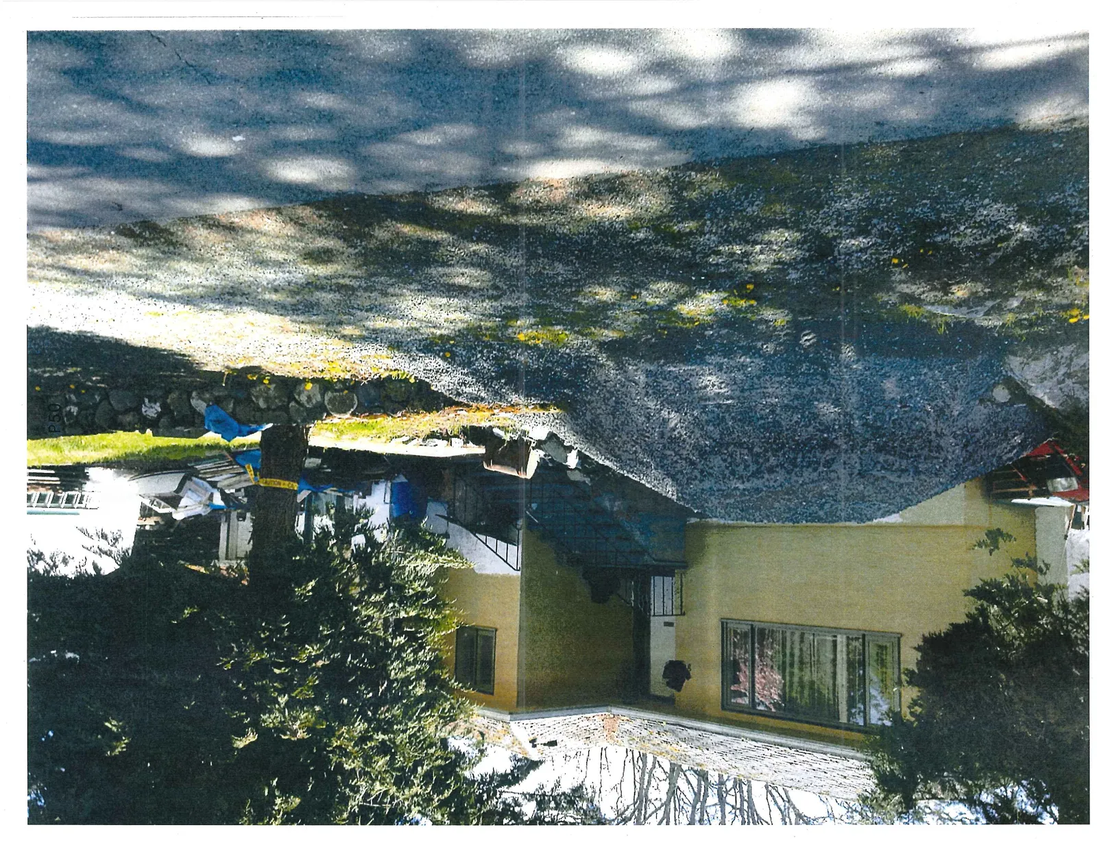 Close-up view of the yellow house and a large pile of gravel on the driveway, with construction materials and debris visible near a tree.