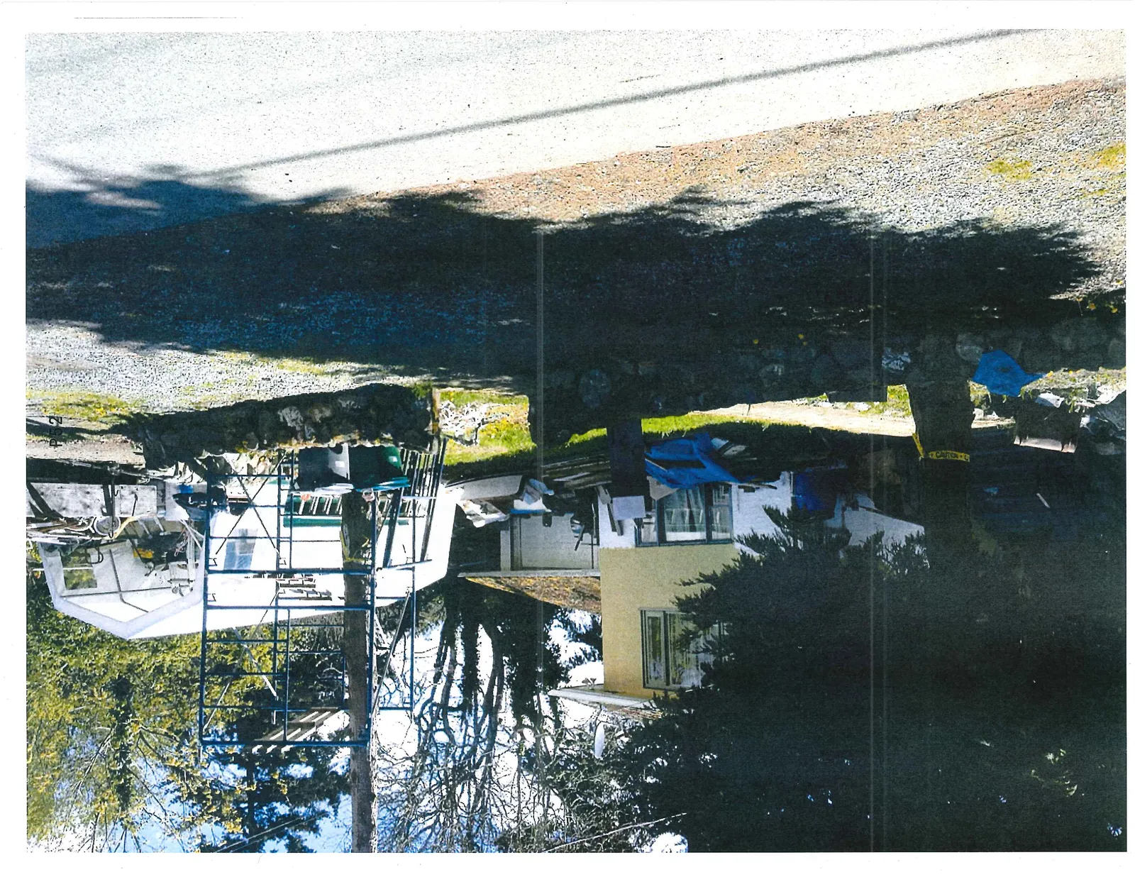 Side view of the property featuring a large white temporary tent structure, metal scaffolding, and additional construction materials next to the yellow house.