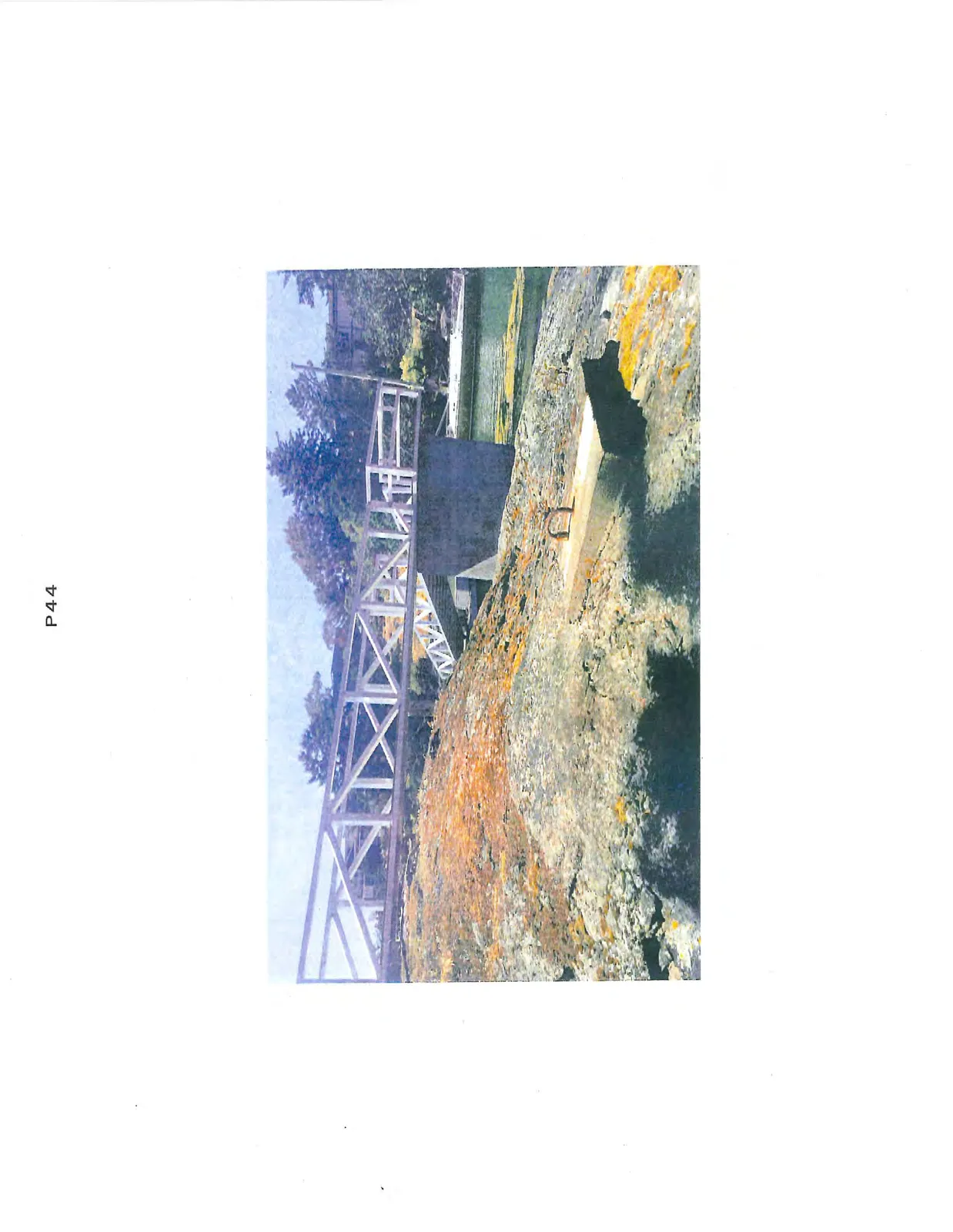 A white wooden pedestrian gangway extending over rocks toward a concrete pier, with a metal mooring ring in the foreground