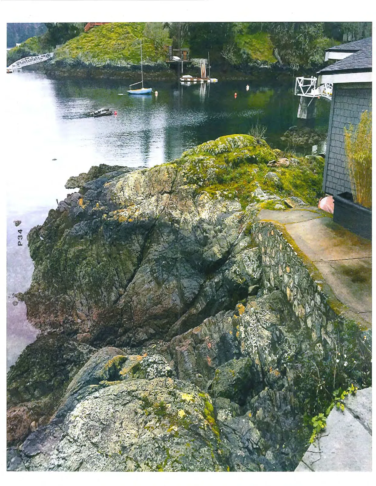Perspective from a stone path toward a rocky point and a bay with small boats.