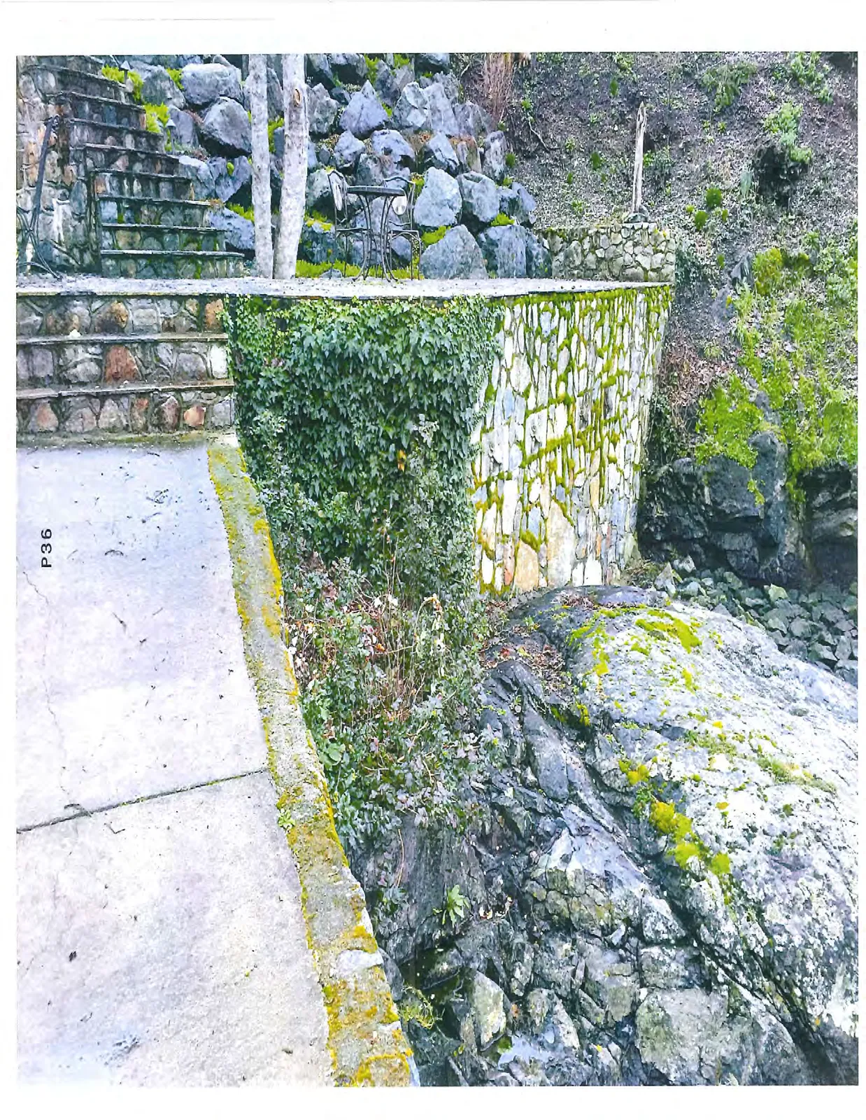 Stone masonry retaining wall with ivy growth, stone steps, and large boulders.