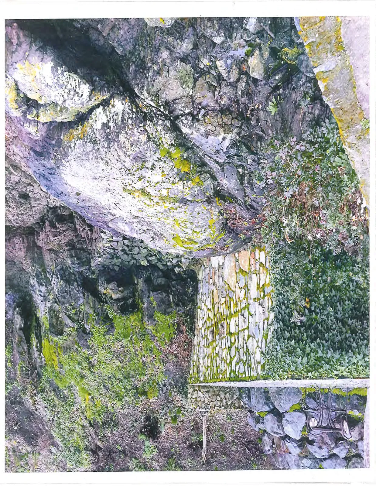 Landscaped stone wall and stairs integrated into a rocky hillside with moss and vegetation.