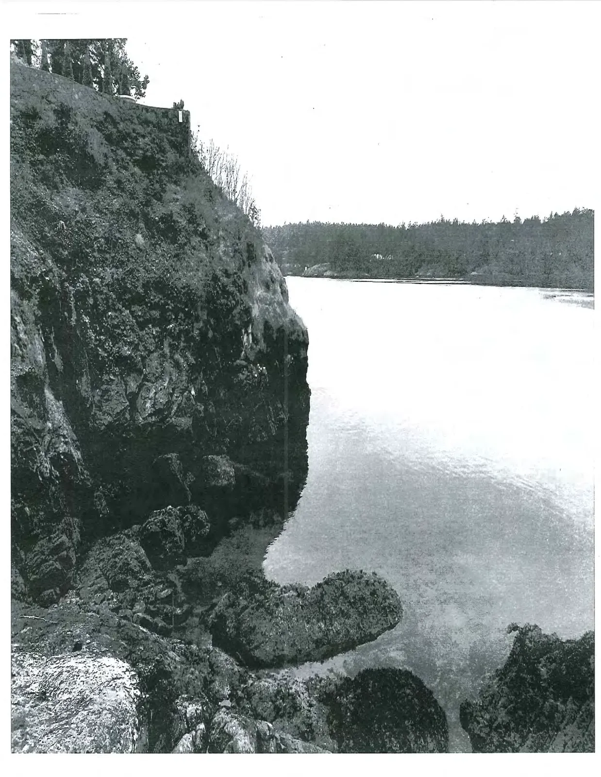Black and white photo of a steep rocky cliff face overlooking a calm body of water.