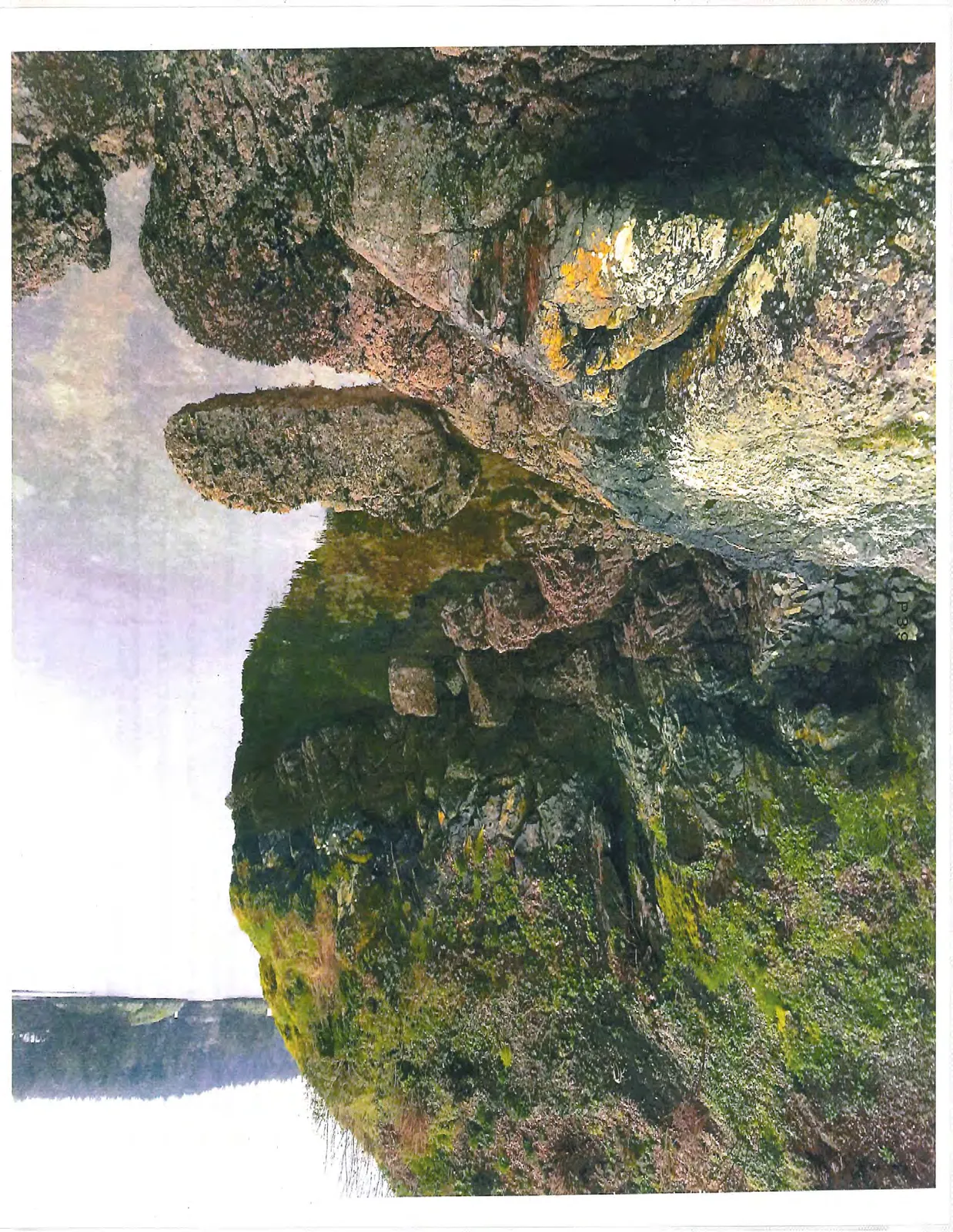 Color photo of a steep, moss-covered rocky cliff by the water.