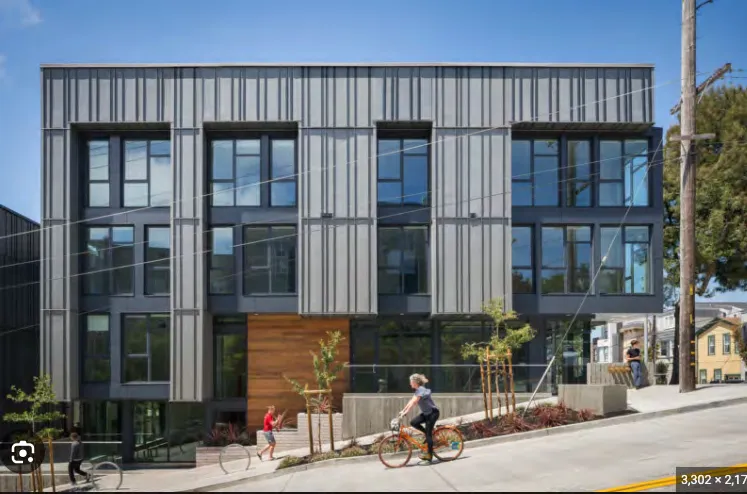 Photo of a contemporary multi-unit residential building with grey vertical siding and dark-framed windows.
