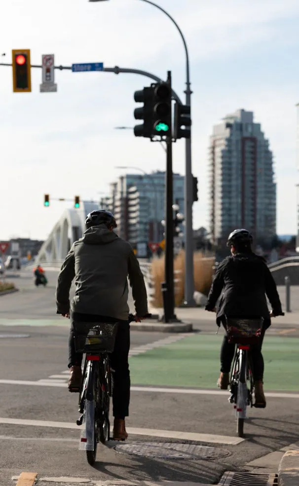 Two people riding bicycles through an urban intersection with a green bike lane and traffic lights
